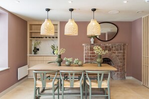 A dining area with a table, chairs, hanging wicker lamps, a brick fireplace, and a mirror on the wall. - Hidden 9- Grand Bay Suite Hot Tub (St Ives)