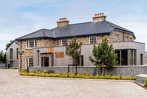 A two-story stone house with a grey roof, large windows, and a wooden front door. - Hidden 9- Grand Bay Suite Hot Tub (St Ives)