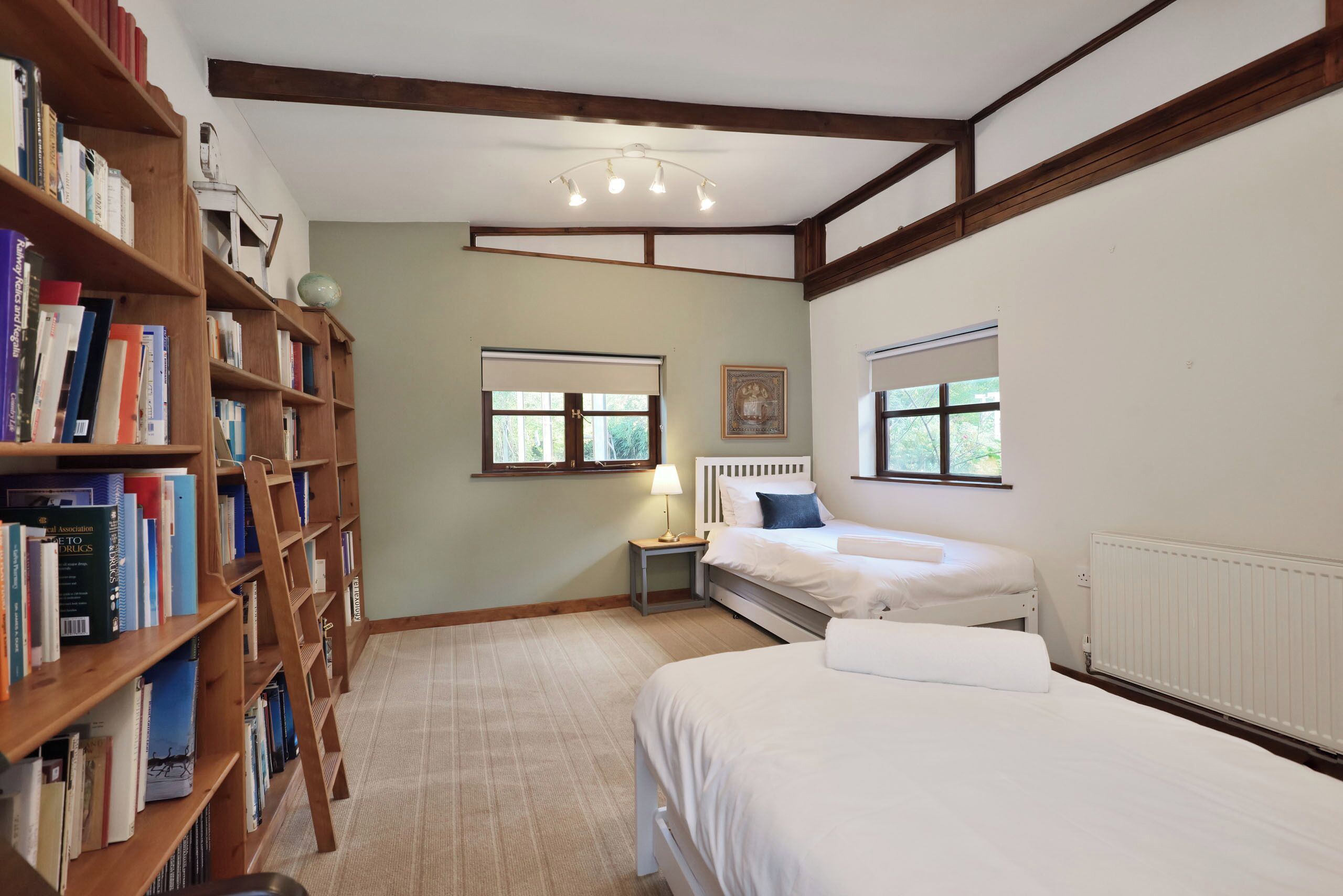A bedroom with a bed, a bedside table, a lamp, a window, and a bookshelf.
