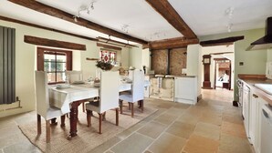 Een ruime keuken met een eethoek, houten balken, stenen vloer en uitzicht op de woonkamer.