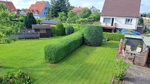 Ein gepflegter Garten mit ordentlich geschnittenen Hecken, einem Holzzaun und einem kleinen Gartenhaus.