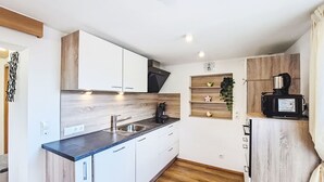 Een kleine keuken met witte kastjes, een zwart aanrecht, een spoelbak, een koffieapparaat en een houten plank met decoratieve objecten.
