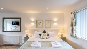 Een slaapkamer met een bed, twee bedlampen, een wandtelevisie, een radiator en twee ingelijste botanische prints aan de muur.