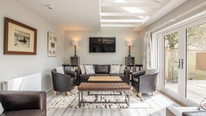 Een moderne woonkamer met een zithoek, een salontafel en een open haard. Er zijn boekenkasten en een groot raam met uitzicht.
