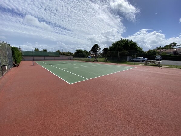 Ein Tennisplatz mit grünem Spielplatz und rotem Umfeld, Bänke und ein Picknicktisch.