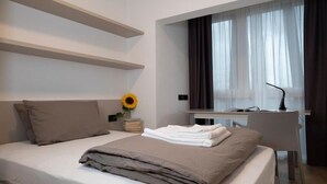 A modern hotel room with a bed, a desk, and a window with curtains. - SILVANELLO Apartment (Trento)