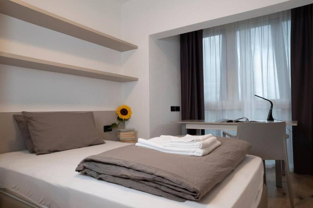 A modern hotel room with a bed, a desk, and a window with curtains.