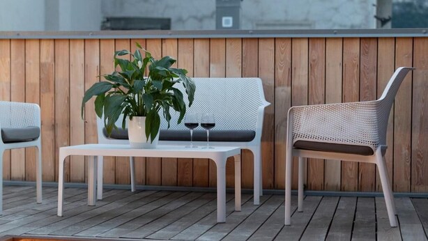 A wooden deck with a white table, two wicker chairs, a potted plant, and two wine glasses. - SILVANELLO Apartment (Trento)