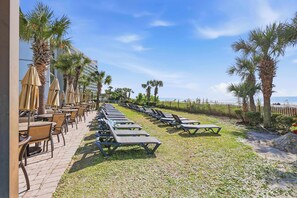 Eine Hotelterrasse direkt am Strand mit Liegestühlen, Sonnenschirmen und Palmen.
