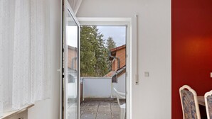 Una stanza con una porta scorrevole in vetro che dà su un balcone con vista su alberi e un edificio.
