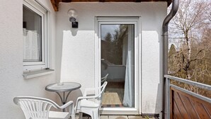 Un balcone con tavolo e sedie, una porta scorrevole in vetro e un recinto in legno.