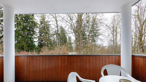 Un portico coperto con tavolo e sedie bianche, una recinzione in legno e alberi sullo sfondo.