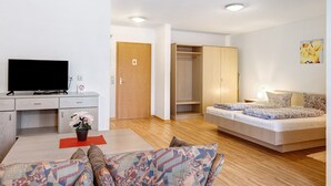 Un soggiorno moderno con una TV a schermo piatto, un divano, un letto, un pavimento in legno e un armadio.