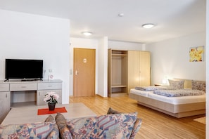 Ein modernes Wohnzimmer mit Flachbildfernseher, einer Couch, einem Bett, Holzboden und einem Schrank.