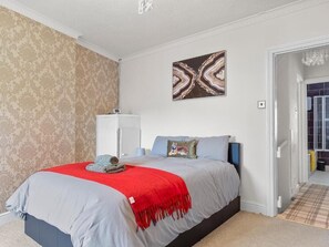 A bedroom with a bed, a red throw blanket, a wall-mounted abstract painting, and a patterned wallpaper. - 3 bed Home Workington Near Lake District (Workington)