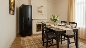 Un coin repas avec une table dressée pour quatre personnes, un réfrigérateur noir, une cheminée et un tableau encadré au mur.