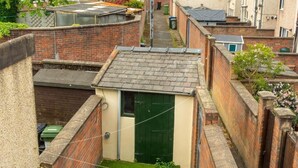 Une ruelle étroite avec une petite porte verte, des murs en briques et un espace herbeux.