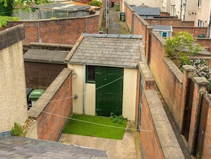 A narrow alleyway with a small green door, brick walls, and a grassy area. - 3 bed Home Workington Near Lake District (Workington)