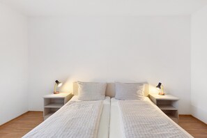 A minimalist bedroom with a double bed, two bedside tables with lamps, and a wooden floor. - Apartment 30, Free DreiWeltenCard & Balcony – Only 2 Minutes from Solemar (Bad Dürrheim)