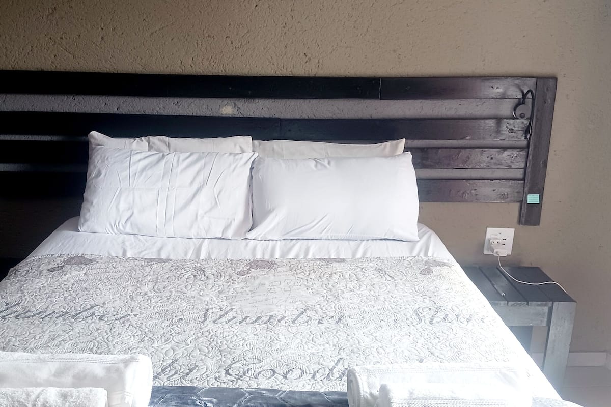 Una cama con cabecera de madera, ropa de cama blanca y una colcha estampada.