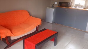 Una sala de estar con sofá, una mesita, una kitchenette con microondas y refrigerador.