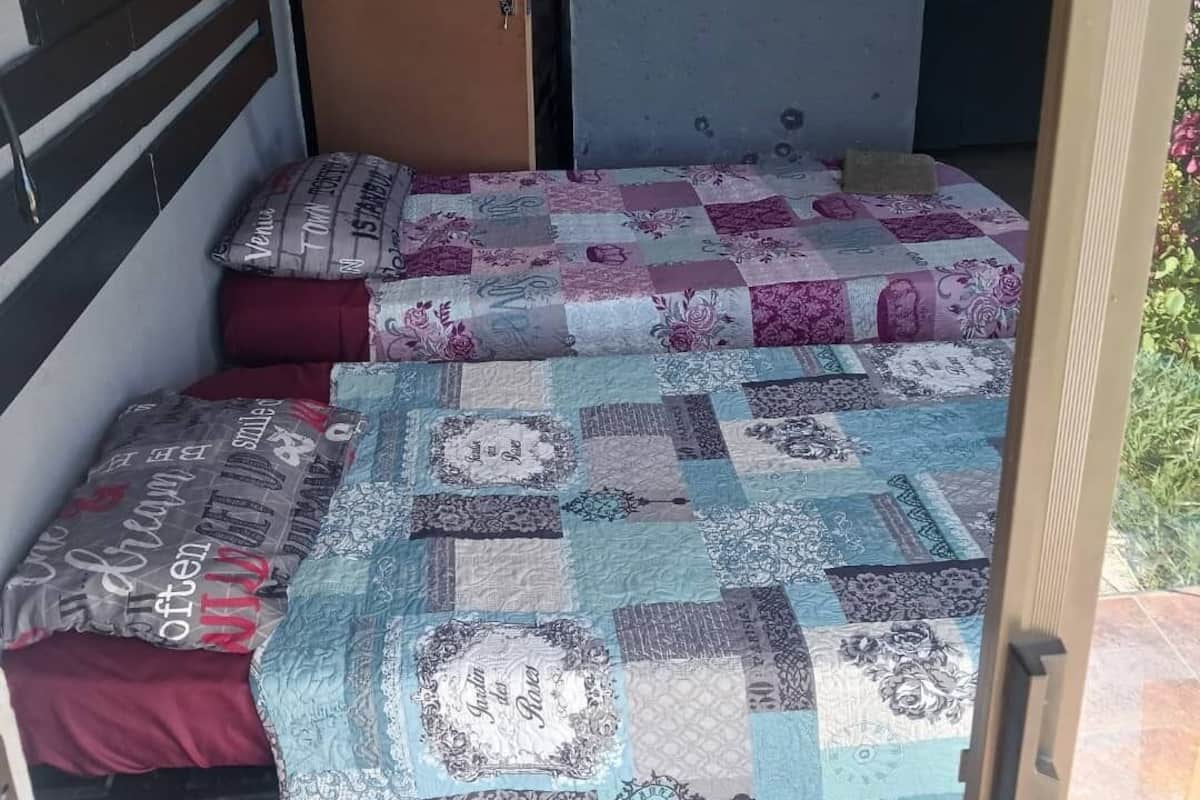 Una habitación compacta con dos camas, cada una con colcha acolchada y almohadas, cabecero de madera y una puerta.