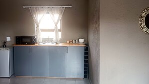 Una kitchenette compacta con microondas, lavamanos y armarios.