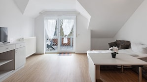 Une pièce moderne et bien éclairée, dotée d’un téléviseur à écran plat, d’une table à manger agrémentée d’une plante en pot, d’un canapé et d’une porte-fenêtre coulissante donnant sur un espace extérieur.