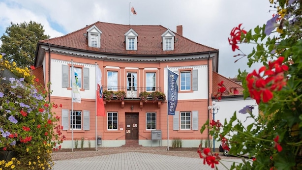 Un bâtiment à deux étages, doté d’une façade symétrique, d’une entrée centrale et d’un drapeau au sommet.