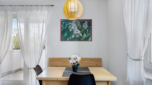 Uma área de refeições com mesa, cadeiras, um vaso com flores, uma luminária pendente e um quadro na parede.