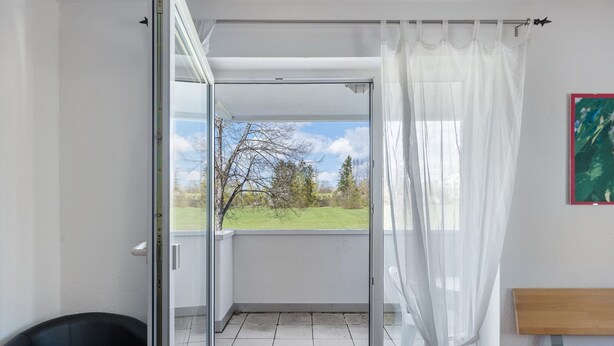 Quarto com porta de vidro que dá para uma varanda, uma cadeira, uma cama e um quadro na parede.