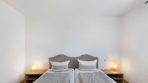 Quarto duplo com duas camas, mesas de cabeceira e luminárias fixadas na parede.