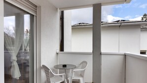 En balkon med et bord og to stole, en skydedør i glas samt en hvid facade.