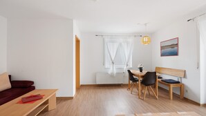 En moderne stue med en træbænk, et spisebord med stole, en rød bordløber og et vindue med lette gardiner.