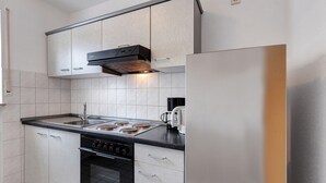 Uma cozinha moderna com geladeira de aço inoxidável, forno embutido, fogão a gás e armários em tons claros.