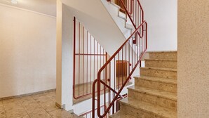 Uma escadaria com corrimão de metal vermelho, paredes bege e piso de azulejos.