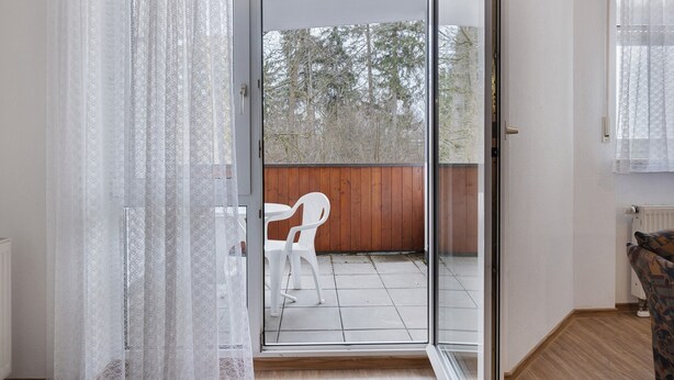 Quarto com porta de vidro deslizante que dá para área externa com cerca de madeira e uma cadeira de plástico branca.