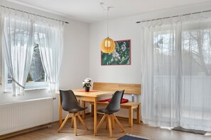 Ein Essbereich mit Holztisch, schwarzen Stühlen, einem roten Kissen, einer Hängeleuchte und einem gerahmten Bild an der Wand.