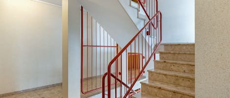 Una escalera con barandillas rojas, paredes color beige y piso de baldosas.