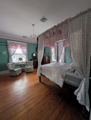A bedroom with a four-poster bed, two chairs, a dresser, and a mirror.