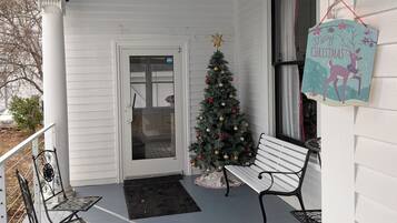 Un portico coperto con una ventola a soffitto, un albero di Natale, due sedie in metallo e una panchina.