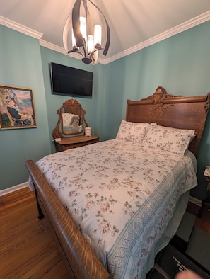 A bedroom with a wooden bed, a nightstand, a television, and a painting on the wall.