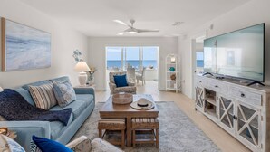 A living room with a sofa, coffee table, TV, and a view of the ocean. - The Happy Turtle at Fisherman's Cove (Siesta Key)