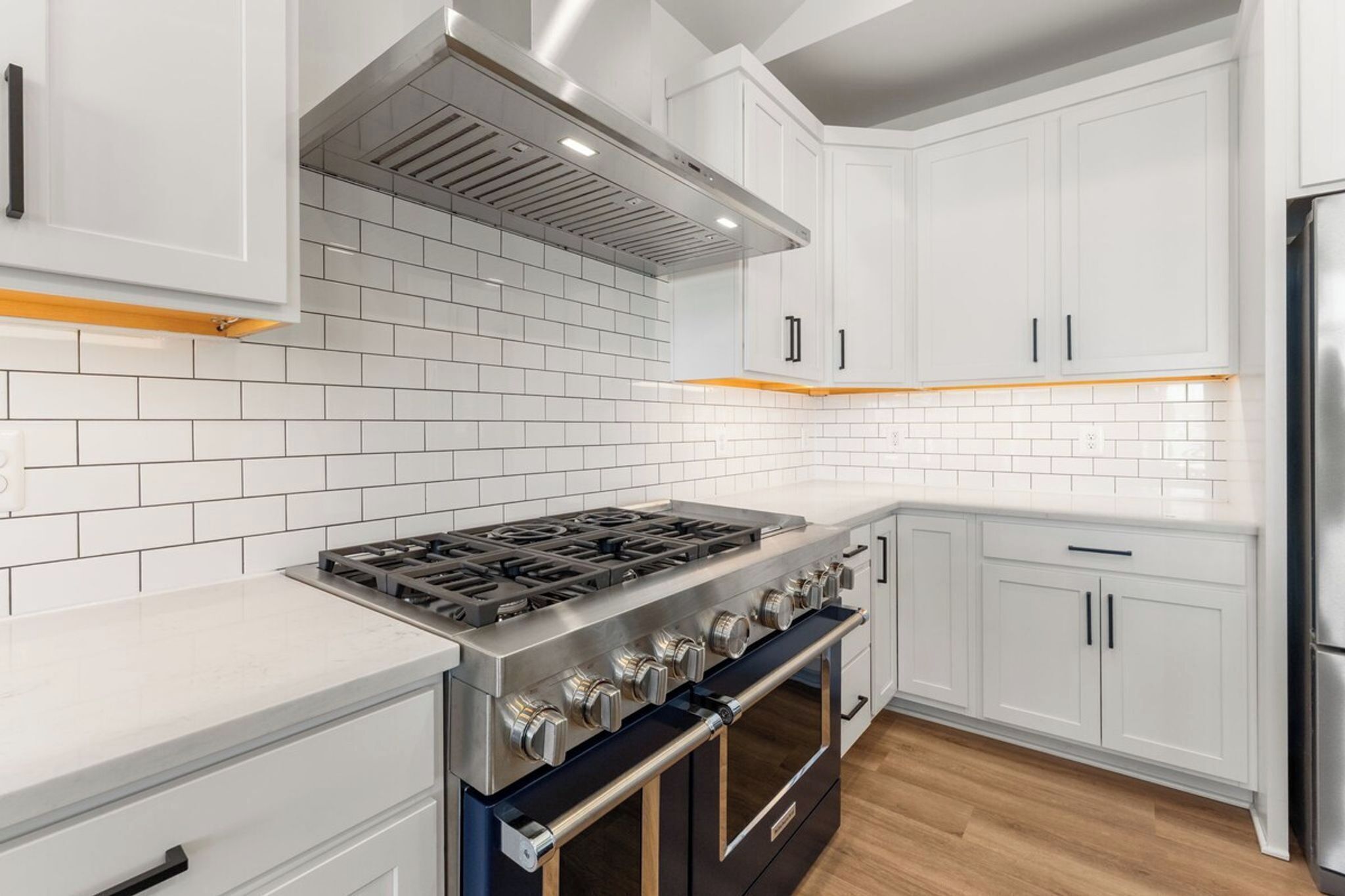 A modern kitchen with white cabinetry, a stainless steel stove, and a built-in oven.