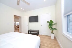 Ein Schlafzimmer mit einem Bett, einer Bank, einem Fernseher, einer Tür und einer Zimmerpflanze.