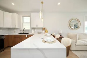 A modern kitchen with white cabinetry, a central island, and a dining area with a sofa and table. - Stylish - mins from airport - Modern - Clean (Boston)