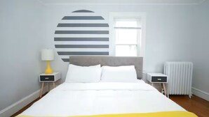 Ein Schlafzimmer mit einem Bett, einem Nachttisch mit Lampe, einem Heizkörper und einem Fenster.