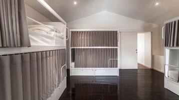 Une chambre moderne avec un lit superposé, une grande fenêtre avec des rideaux et un plancher en bois foncé.