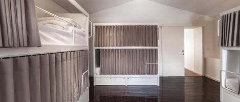 A modern room with a bunk bed, a large window with curtains, and a dark wooden floor.