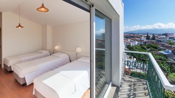 A modern hotel room with two beds, a balcony with a view of the city, and a large window. - A Bica Hostel (Ponta Delgada)